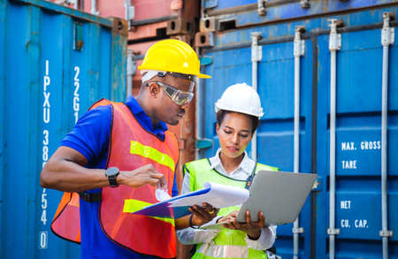 Worker man in hardhat and safety vest holding clipboard checklist and Female foreman using laptop...