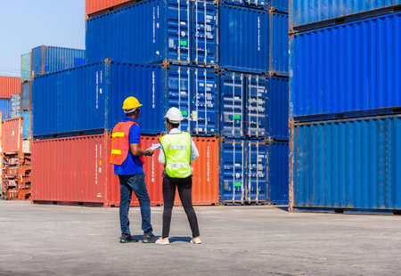 Female foreman with safety vest holding laptop and  worker man in hardhat checking and control loading containers box from cargoの写真素材