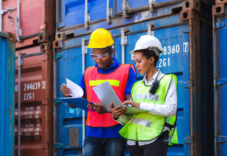 Happy worker man in hardhat and safety vest holding clipboard checklist and Female foreman using laptop control loading containers box from cargoの写真素材