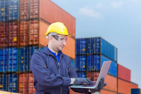 Engineer with clipping path in hardhat and safety vest holding laptop, Foreman control loading containers box from cargoの写真素材