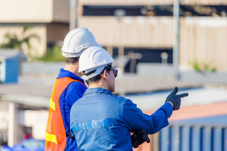 Worker man in hardhat and safety vest and foreman checking control loading containers box from cargo, Teamwork conceptの写真素材