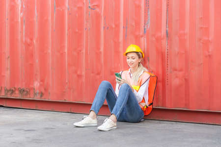 Female engineer in the hard hat uses mobile phone, Industrial worker using mobile smartphone in industry containers cargoの写真素材