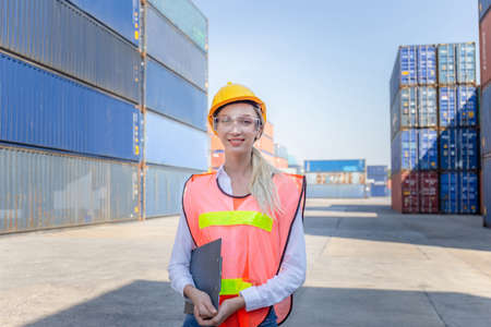 Cheerful female shipping company workers working at the harbor, Women engineer smiling in hardhat and safety vest holding clipboard checklist at cargo containers backgroundの写真素材