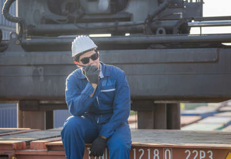 Foreman in hardhat and safety vest talks on two-way radio control loading containers box from cargo