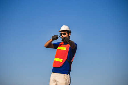 Factory worker in hardhat and safety vest holding two-way radio and pointing forward