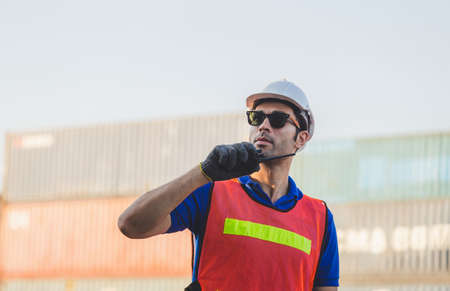 Happy foreman in hardhat and safety vest talks on two-way radio control loading containers box from...