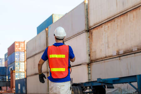 Foreman in hardhat and safety vest talks on two-way radio control loading containers box from cargoの写真素材