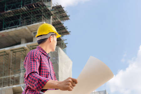 Engineer man with clipping path checking and planning project at construction site, Man holding blueprint and looking into the skyの写真素材