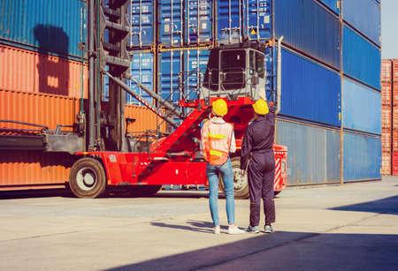 Worker man in hardhat and safety vest holding laptop and Female engineer control loading containers box from cargoの写真素材