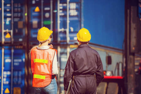 Worker man in hardhat and safety vest holding laptop and Female engineer control loading containers box from cargoの写真素材