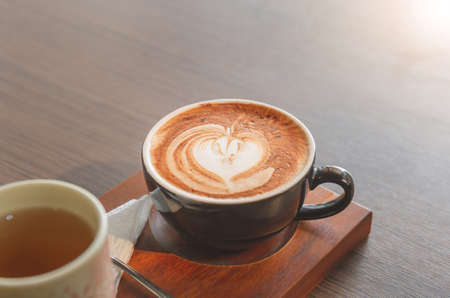 Hot latte art coffee in ceramic cup with tea cup on wooden table backgroundの写真素材