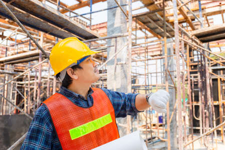 Engineer / foreman checking and planning project at construction site, Man holding blueprint with blurred backgroundの写真素材