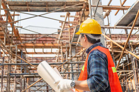 Worker man in hard hat holding blueprint checking and planning project at construction siteの写真素材