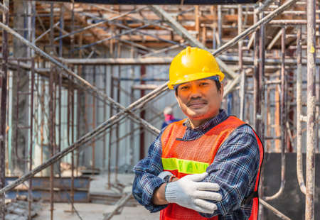 Worker checking and planning project at construction site, Smiling man with arms crossed over blurred backgroundの写真素材