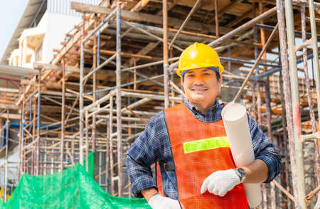 Engineer man checking and planning project at construction site, Smiling man holding paper blueprint and looking to cameraの写真素材