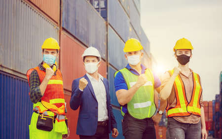 Success and Teamwork Concept, Engineer and worker team wearing protection face mask against coronavirus, Happy business people team celebration with blurred cargo containers backgroundの写真素材