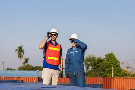Factory worker man in hard hat and safety vest and foreman checking control loading containers box from cargo, Teamwork conceptの写真素材