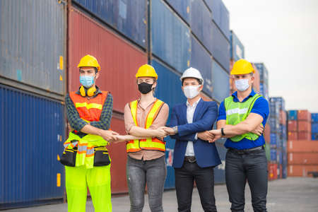 Factory worker and engineer team wearing protection face mask, Team holding hands and standing in row at cargo containersの写真素材