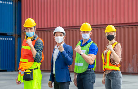 Engineer and worker team wearing protection face mask against coronavirus, Happy business people team celebration with blurred cargo containers backgroundの写真素材