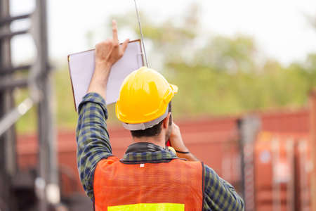 Foreman worker in hardhat and safety vest talks on two-way radio control loading containers box from...
