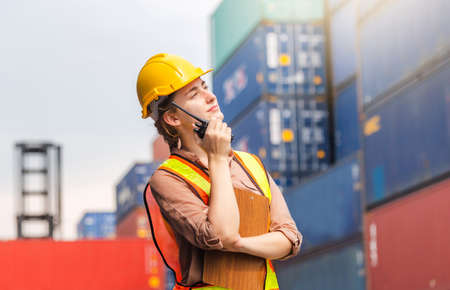 Engineer in hardhat and safety vest holding clipboard checklist and two-way radio at containers...