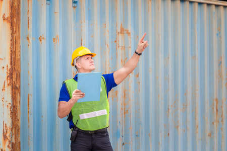 Engineer man in hard hat holding clipboard checklist and pointing to the sky at container cargo