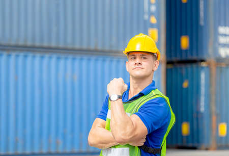 Happiness foreman worker in hardhat show strong arm muscles at containers cargoの写真素材