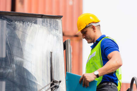 Worker man in hard hat and safety vest standing on container stackers control loading containers box from cargoの写真素材