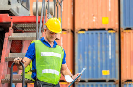 Worker man in hardhat and safety vest standing on container stackers control loading containers box...