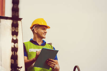 Engineer man in hard hat and safety vest standing on container stackers control loading containers...