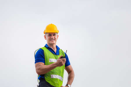 Foreman worker in hardhat and safety vest standing on container box holding two-way radio control...