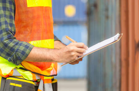 Close up of Worker man holding clipboard checklist and checking containers box from cargoの写真素材