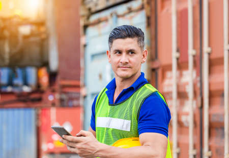 Engineer man uses mobile phone, Industrial worker using mobile smartphone in industry containers cargoの写真素材