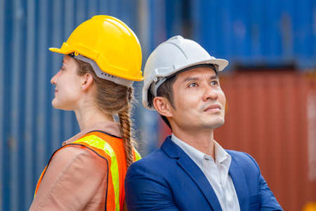 Cheerful factory worker team in hard hat smiling with arms crossed at cargo containersの写真素材