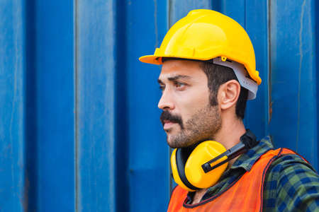 Factory worker man in hard hat and noise reduction ear muffs with containers box backgroundの写真素材