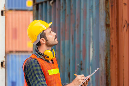 Factory worker man in hard hat holding clipboard checklist and checking containers box from cargo
