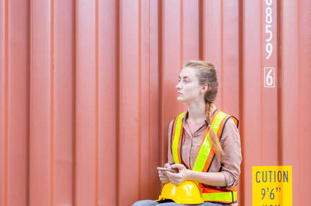 Female engineer holding mobile phone, Industrial worker sitting alone and holding smartphone in...