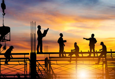 Silhouette of Engineer and worker on building site, construction site at sunset in evening time.の写真素材