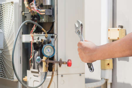 Technician man hands holding a wrench over blurred modern air conditioning, Maintenance and repairing conceptの写真素材