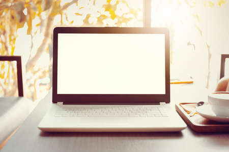 Blank screen of Laptop with a coffee cup on wooden table blurred background.