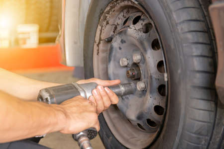 Close up of repair mechanic hands during maintenance work to pneumatic gun to loosen a wheel nut changing tyre of carの写真素材