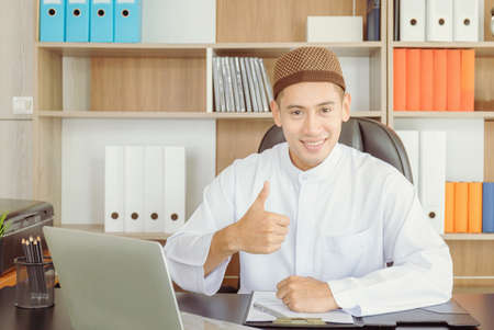 Selective focus of Happy young business arab middle eastern muslim man in office and showing thumb upの写真素材