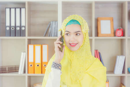 Selective focus of Smiling young business arab middle eastern muslim woman using smartphone in officeの写真素材