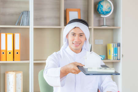Selective focus of Young business arab middle eastern muslim holding clipboard with house model and money banknote. Saving and investment to real estate conceptの写真素材