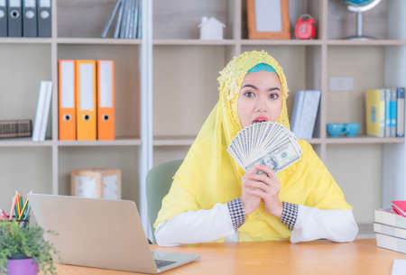 Selective focus of young business muslim woman holding and showing money banknotes, Arab finance concept.の写真素材