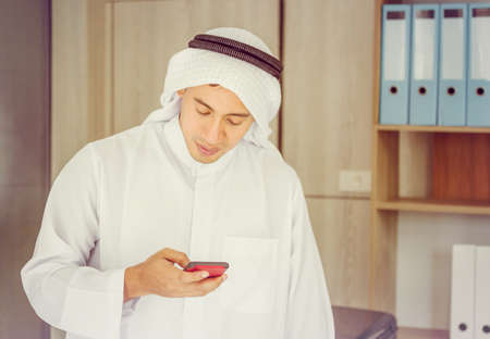 Close up of young Arab Middle Eastern Businessman using mobile smartphone in officeの写真素材