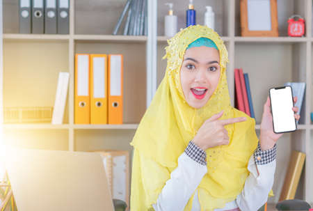 Selective focus of Young business arab middle eastern muslim woman showing blank screen mobile smart phoneの写真素材