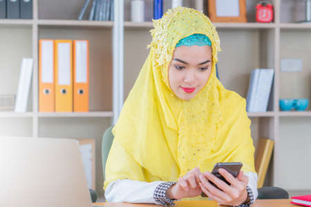 Selective focus of Smiling young business arab middle eastern muslim woman using smartphone in officeの写真素材