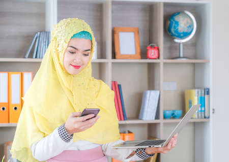 Smiling young business arab middle eastern muslim woman using smartphone and laptop, Work form home conceptの写真素材