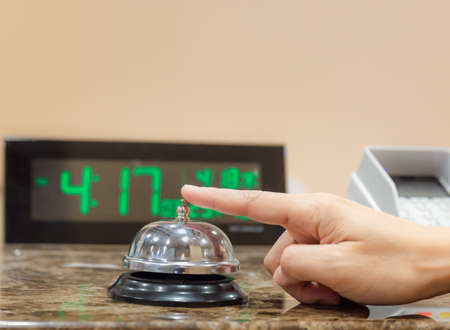 Female hand ringing a service bell on hotel reception counter, travel concepts